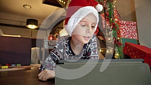 Little boy in Santa's cap lying on floor and using tablet computer on Christmas