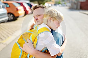 Little boy says goodbye and hugging to his father before going to school. Dad brought his son by car. Education for children.