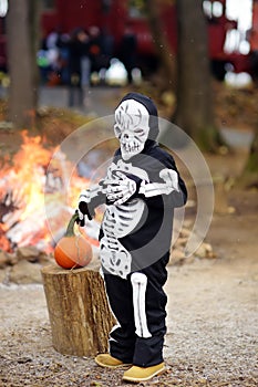 Little boy in scary skeleton costume on background of bonfire at halloween celebrations party in forest