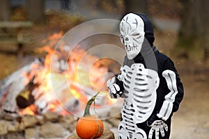 Little boy in scary skeleton costume on background of bonfire at halloween celebrations party in forest