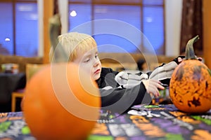 Little boy in scary skeleton costume paints pumpkin on halloween party for children