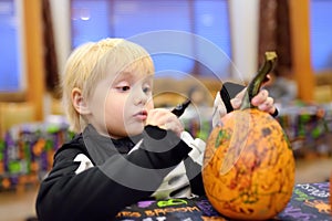 Little boy in scary skeleton costume paints pumpkin on halloween party for children