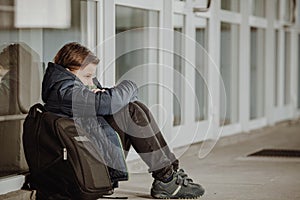 Little boy or school child sitting alone on floor in front of the school after suffering an act of bullying