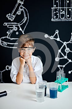 Little boy scientist in lab coat adjusting eyeglasses isolated on black