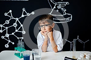 Little boy scientist in lab coat adjusting eyeglasses isolated on black