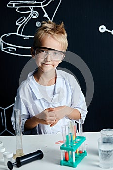 Little boy scientist in lab coat adjusting eyeglasses isolated on black