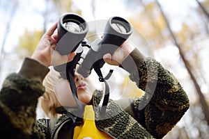 Little boy scout with binoculars during hiking in autumn forest. Child is looking through a binoculars