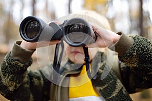 Little boy scout with binoculars during hiking in autumn forest. Child is looking through a binoculars