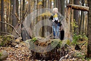 Little boy scout with binoculars during hiking in autumn forest. Child is looking through a binoculars