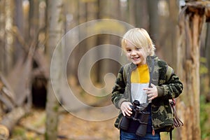 Little boy scout with binoculars during hiking in autumn forest. Child is looking through a binoculars