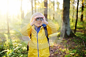 Little boy scout with binoculars during hiking in autumn forest. Child is looking with binoculars