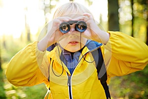 Little boy scout with binoculars during hiking in autumn forest. Child is looking with binoculars