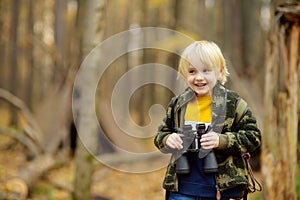 Little boy scout with binoculars during hiking in autumn forest. Child is looking through a binoculars. Behind the baby is teepee