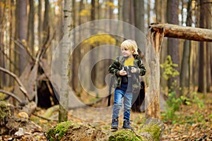 Little boy scout with binoculars during hiking in autumn forest. Child is looking through a binoculars. Behind the baby is teepee