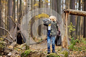 Little boy scout with binoculars during hiking in autumn forest. Child is looking through a binoculars. Behind the child is teepee