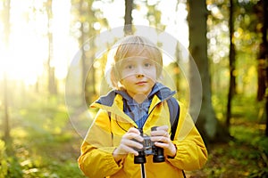 Little boy scout with binoculars during hiking in autumn forest. Child is looking with binoculars. Exploring nature