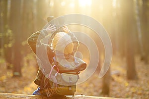 Little boy scout with binoculars during hiking in autumn forest. Child is sitting on large fallen tree and looking through a