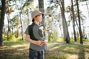 Little boy scout with binoculars during hiking in autumn forest. Concepts of adventure, scouting and hiking tourism for