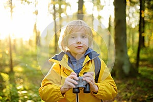 Little boy scout with binoculars during hiking in autumn forest. Concepts of adventure, scouting and hiking tourism for kids