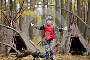 Little boy scout during hiking in autumn forest. Behind the child is teepee hut. Adventure, scouting and hiking tourism for kids