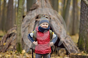 Little boy scout during hiking in autumn forest. Behind the child is teepee hut. Adventure, scouting and hiking tourism for kids