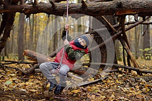 Little boy scout during hiking in autumn forest. Child is swinging on bungee. Adventure, scouting and hiking tourism for kids