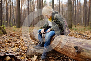 Little boy scout is sharpening a stick with the help knife in the forest