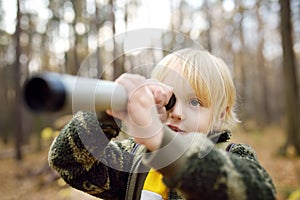 Little boy scout with spyglass during hiking in autumn forest. Child is looking through a spyglass
