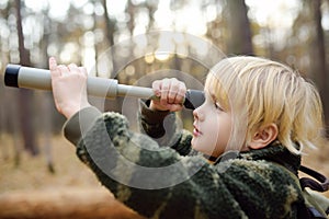 Little boy scout with spyglass during hiking in autumn forest. Child looking through a spyglass. Baby exploring nature. Concepts