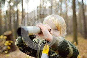 Little boy scout with spyglass during hiking in autumn forest. Child is looking through a spyglass. Concepts of adventure,