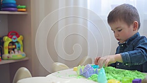 Little boy sculpts from green kinetic sand castles and towers