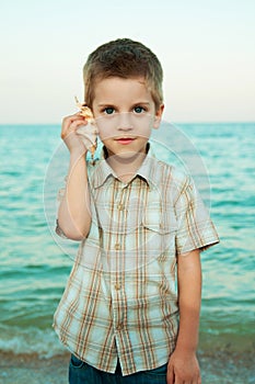 Little boy with a shell on the evening beach.