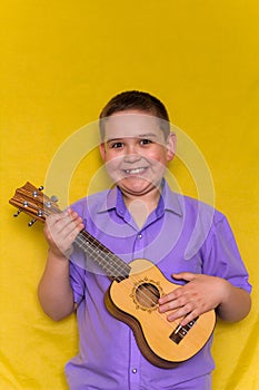 Little boy in  shirt  plays on hawaiian guitar or ukulele iolated on yellow background