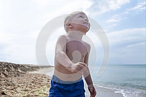 A little boy in shorts runs along the seashore, smiles and looks up. Blue sky on a sunny day. Holidays at the resort and travel.