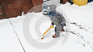 Little boy with a shovel playing outside in the snow. Toddler baby in warm clothes. Little helper concept