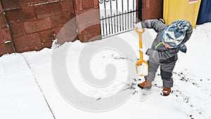 Little boy with a shovel playing outside in the snow. Toddler baby in warm clothes. Little helper concept