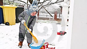 Little boy with a shovel playing outside in the snow. Toddler baby in warm clothes. Little helper concept