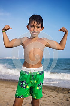 Little boy showing muscles on the beach