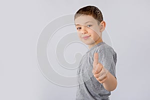 Little boy showing thumb up gesture in a gray T-shirt on white background.