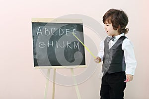 Little boy shows by pointer letters at chalkboard
