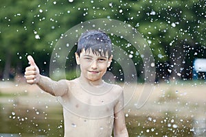 A little boy shows a thumbs up like in the middle of frozen water droplets in the air