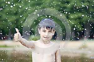 A little boy shows a thumbs up like in the middle of frozen water droplets in the air