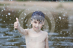 A little boy shows a thumbs up like in the middle of frozen water droplets in the air