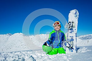 Little boy sit with snowboard in snow hold helmet