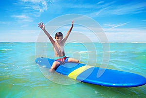 Little boy sit on surfboard with lifted hands up photo