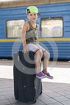 A little boy siting on a big black suitcase at the station. Concept of travel and adventure. vertical photo