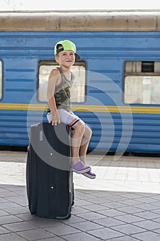 A little boy siting on a big black suitcase at the station. Concept of travel and adventure. vertical photo