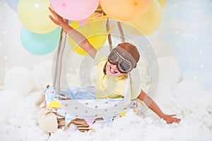 A little boy sits in a balloon basket in the clouds, pretending to travel and fly with an Aviator hat for a concept of creativity