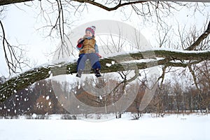 Little boy sits on branch of tree among fallen