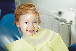 Little boy sits on dentist`s chair in good mood after dental procedures. Young patient with healthy teeth.